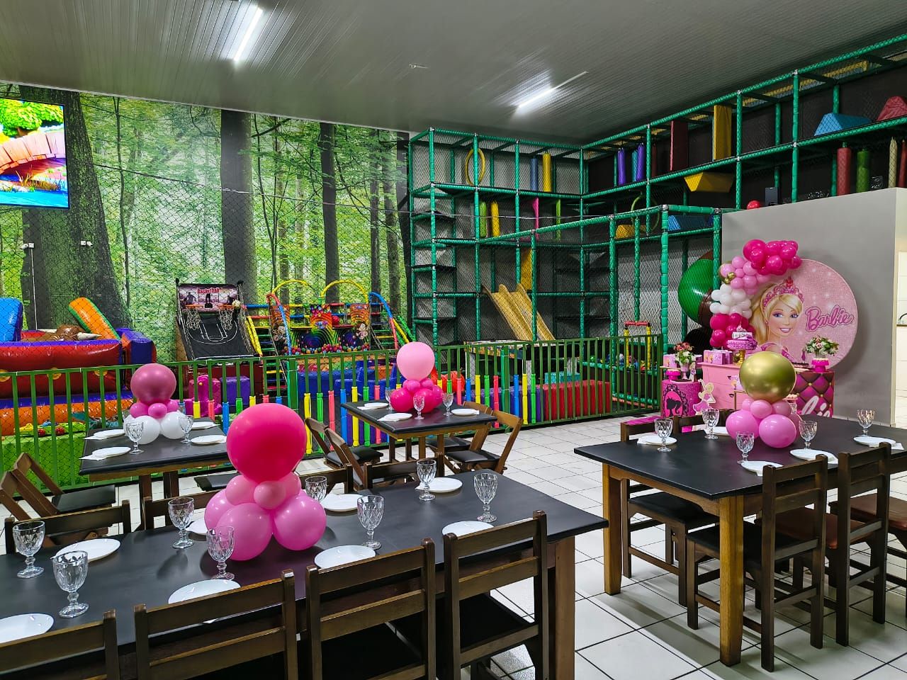 Salão decorado em rosa para festa infantil, com mesas postas e o playground colorido atrás do gradil