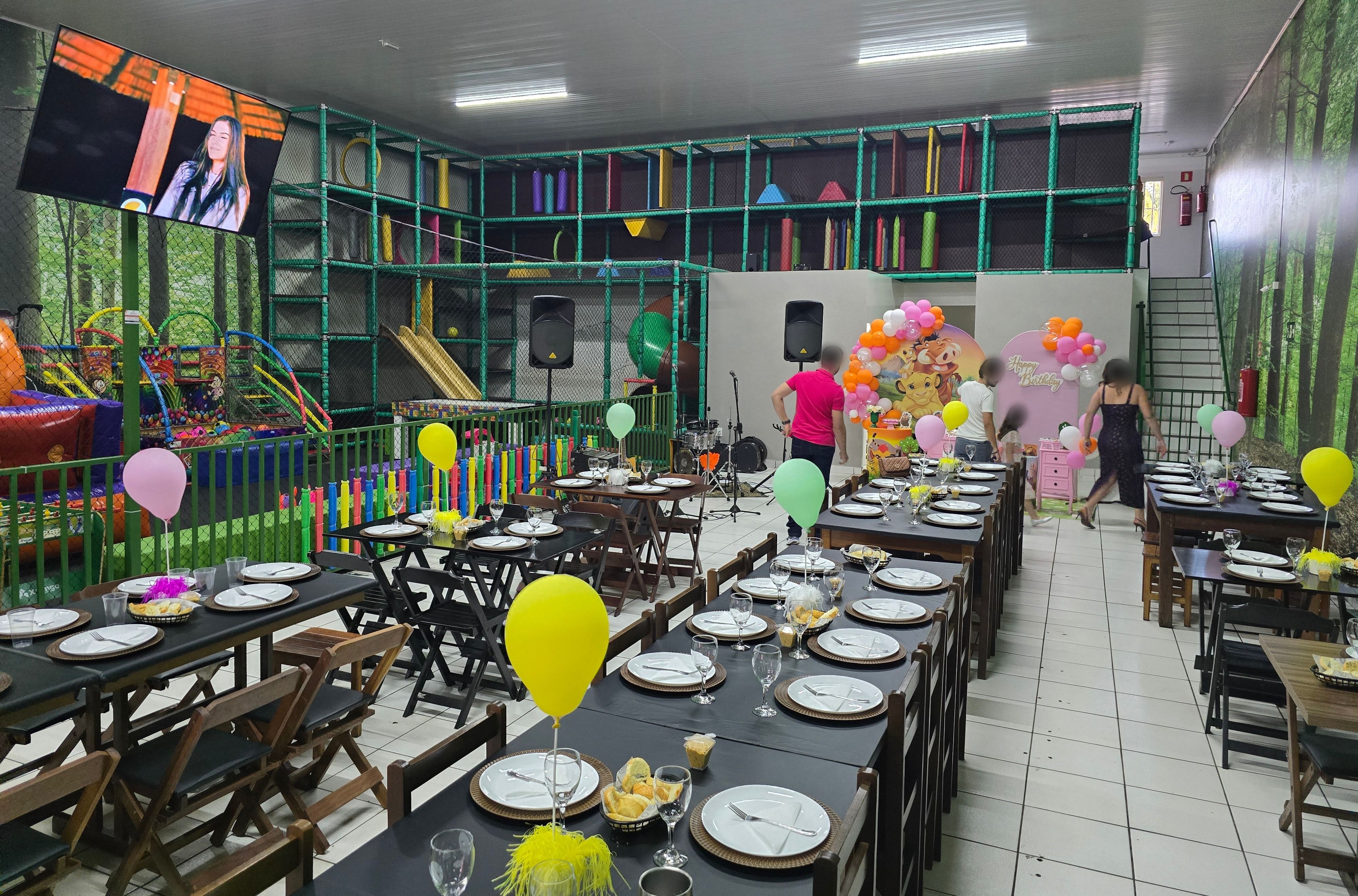 Salão do Espaço Pais & Filhos montado para festa infantil, com mesas postas, playground coberto à esquerda e a TV de 65 polegadas na parede